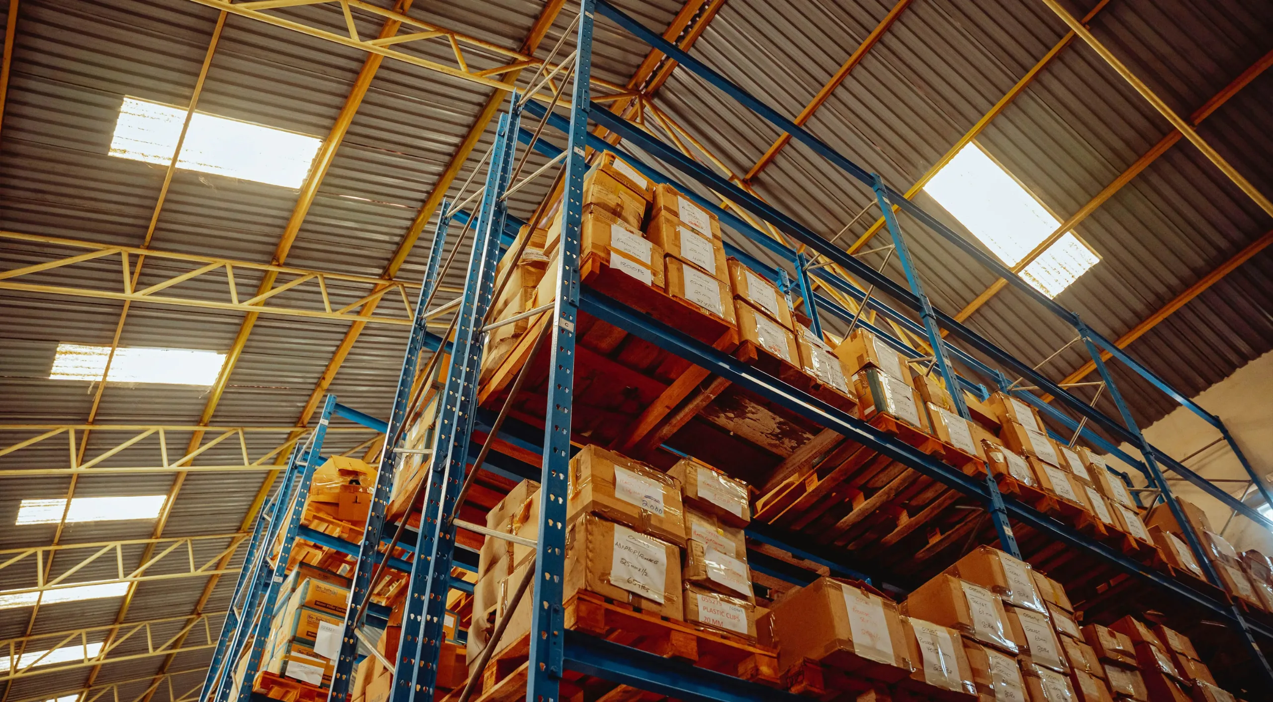 Cardboard cartons on wooden pallets in tall blue warehouse racking